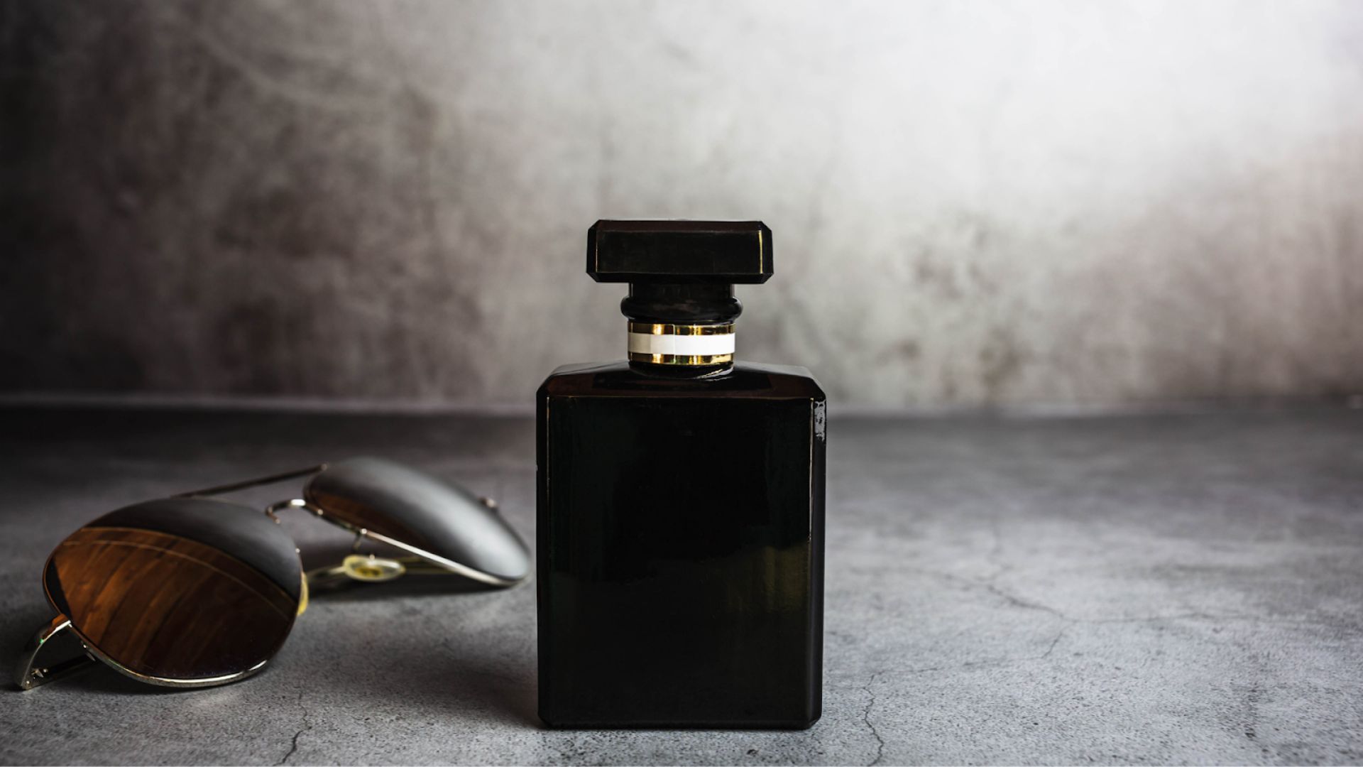 Foto botol parfum berwarna gelap dan kacamata hitam