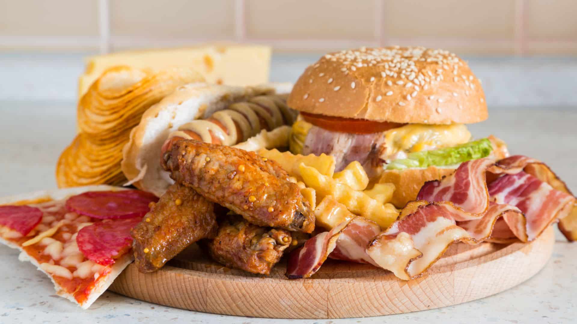 Berbagai junk food di atas piring kayu, pizza, hamburger, sosis, bacon