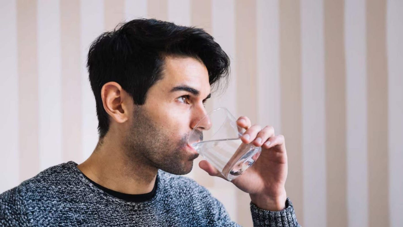 seorang pria yang sedang minum segelas air putih